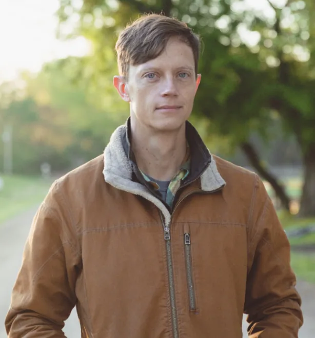 Rob Sand in a brown work jacket on a tree-lined country road